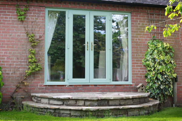 Green French doors on a brick house with steps leading to a garden