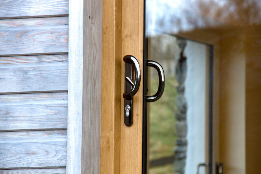 Close-up of an oak-effect sliding patio door with a black handle and key lock, set against timber cladding.